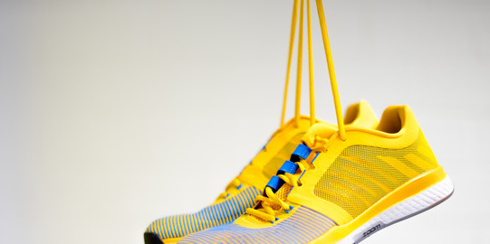 Gelbe Sportschuhe gehalten an den Schnürsenkeln