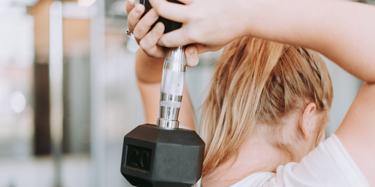 Frau hält Kurzhantel hinter dem Rücken