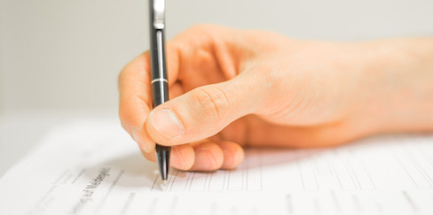 Hand mit Stift beim Formular ausfüllen