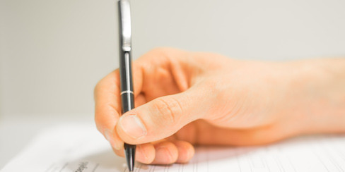 Hand mit Stift beim Formular ausfüllen